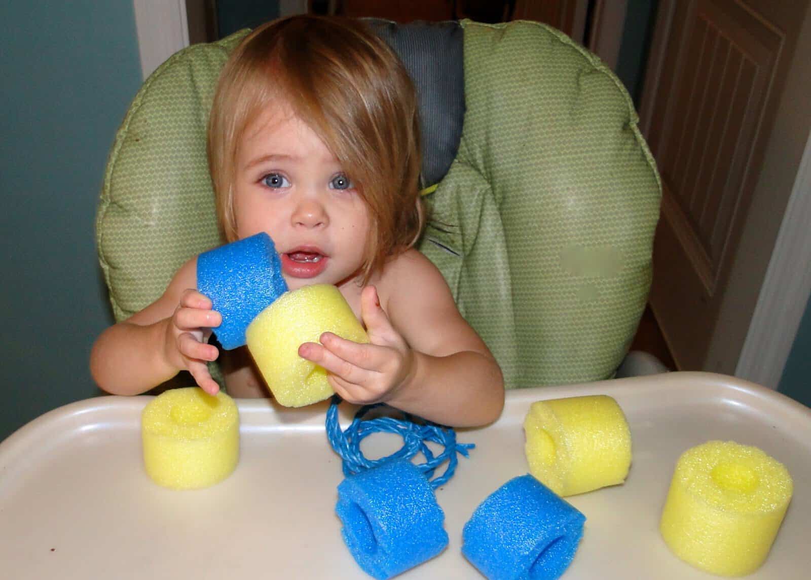 toddler girl playing with pool noodles