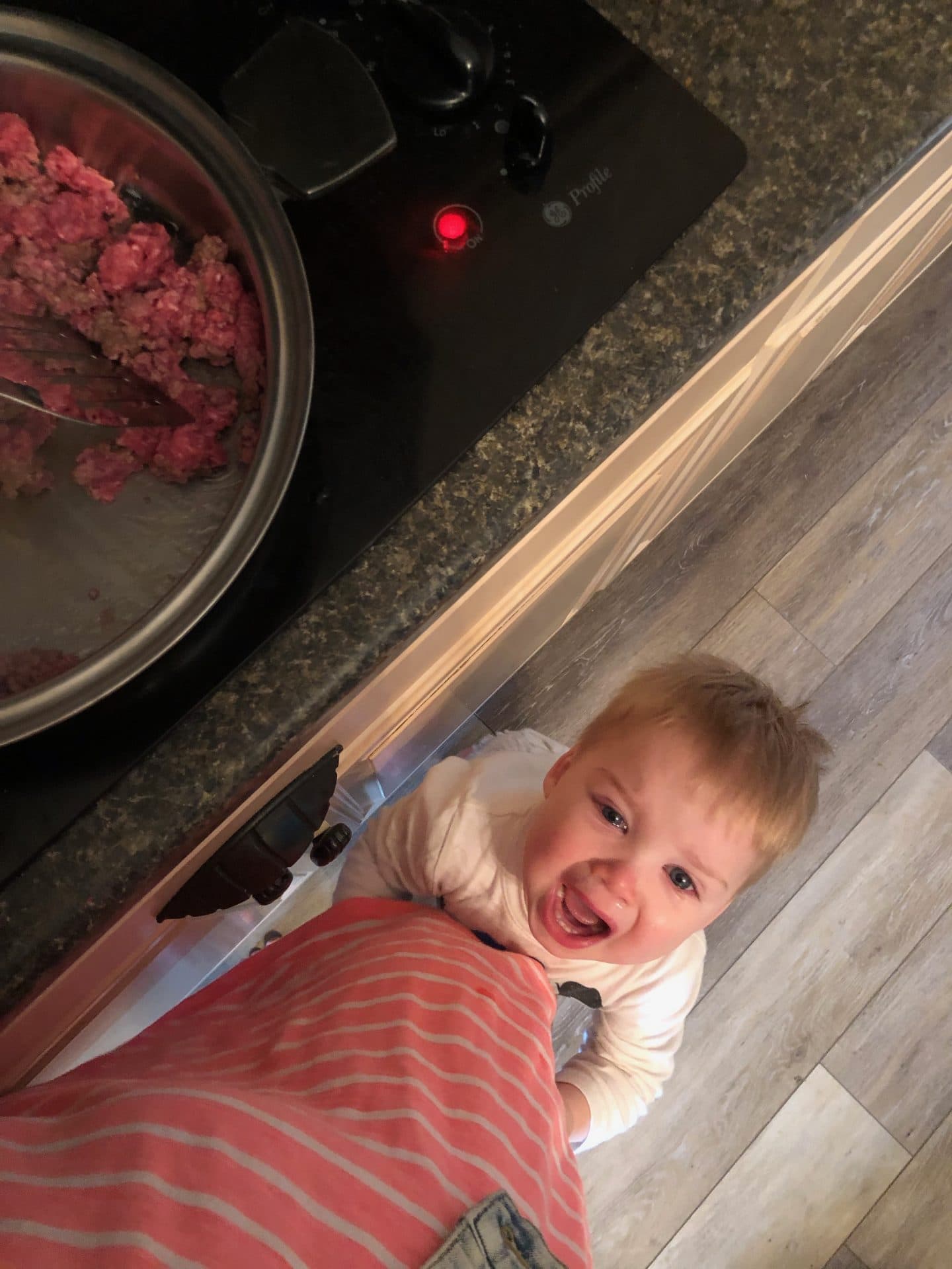 toddler clinging to mom leg while cooking