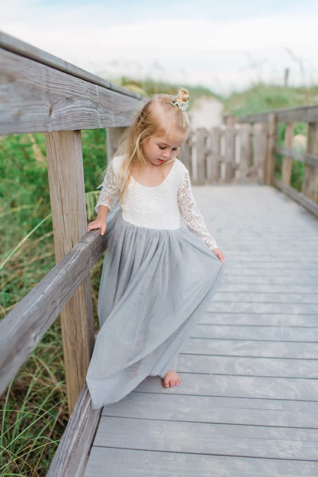 little girl holding dress on the boardwalk at the beach