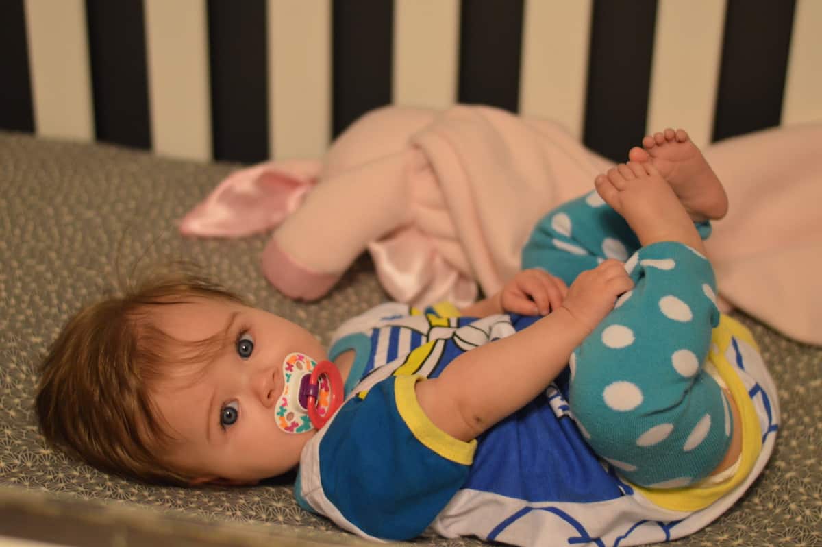 baby laying in crib with pacifier - tips for using pacifier to help baby sleep